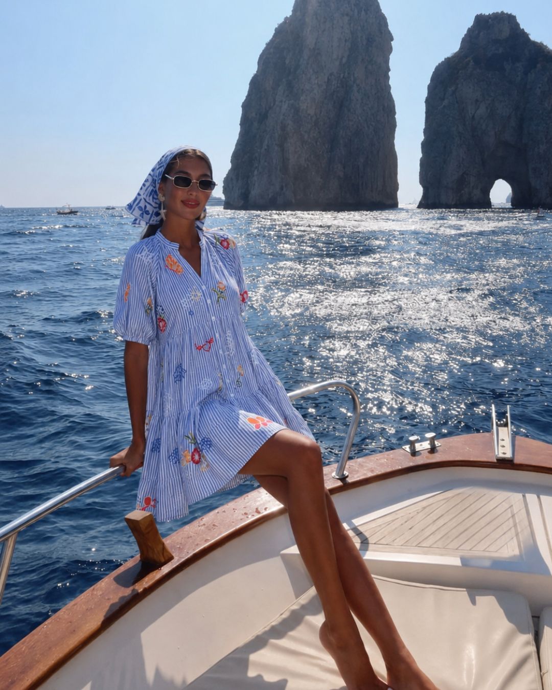 Woman in a blue floral dress on a boat with rock formations in the background